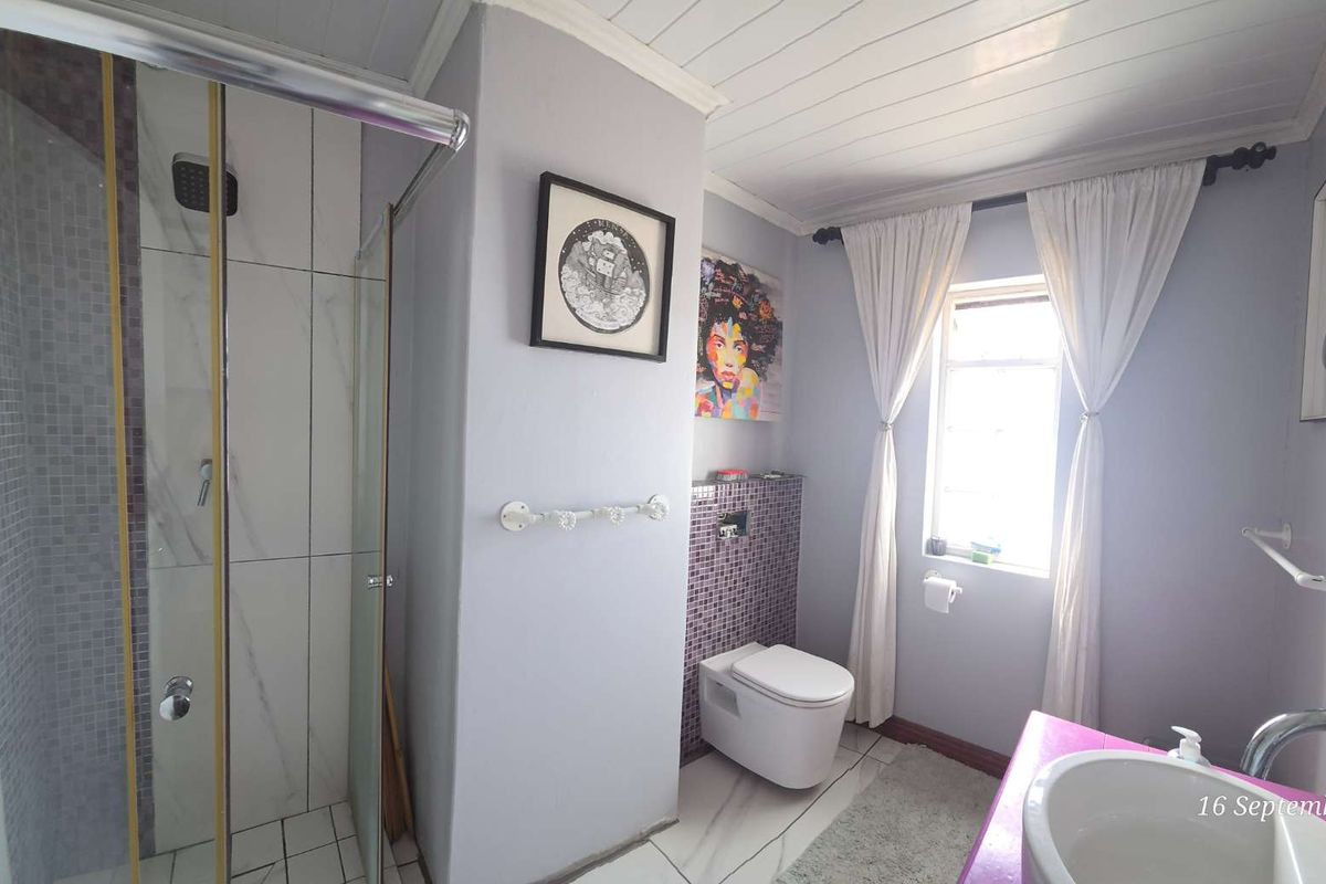 A functional bathroom featuring a glass-enclosed shower, wall-mounted toilet, and a basin with a mixer tap, finished with tiled accents and a tongue and groove ceiling.