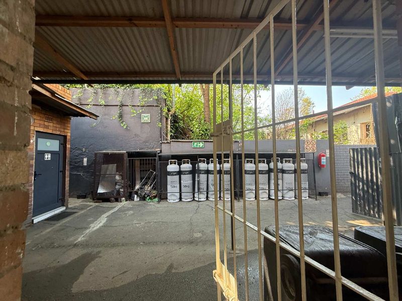 A functional outdoor utility and gas storage area featuring a covered roof, security gate, and designated safety equipment.