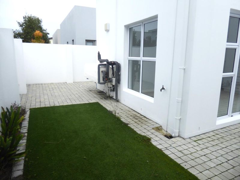A private rear courtyard featuring paved areas, artificial grass, a boundary wall, and an external heat pump unit.