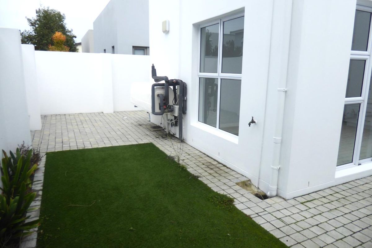 A private rear courtyard featuring paved areas, artificial grass, a boundary wall, and an external heat pump unit.