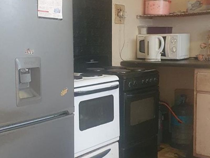 A dated kitchen area featuring a freestanding stove, countertop space, and an exposed electrical distribution board, requiring significant maintenance and cosmetic updates.