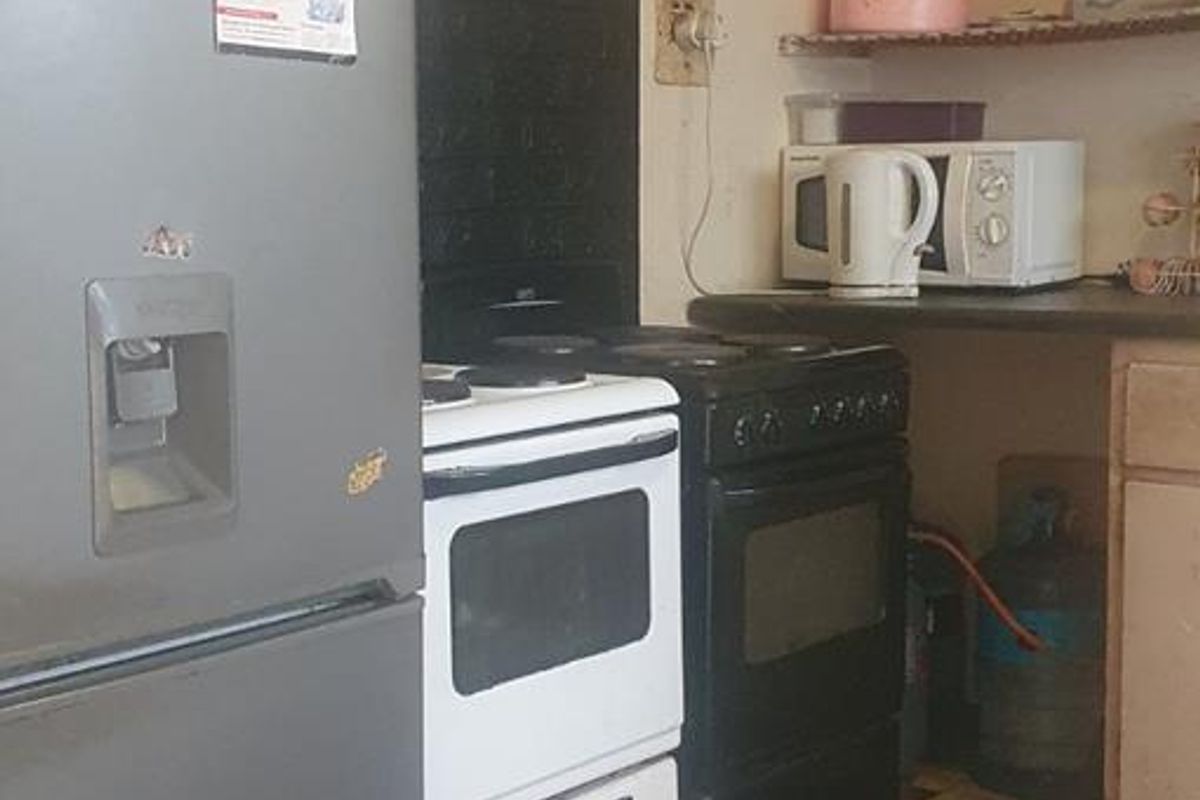 A dated kitchen area featuring a freestanding stove, countertop space, and an exposed electrical distribution board, requiring significant maintenance and cosmetic updates.