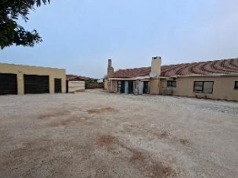 Rear view of the property featuring a tiled roof, chimney, and a large concrete driveway area leading to a detached garage.