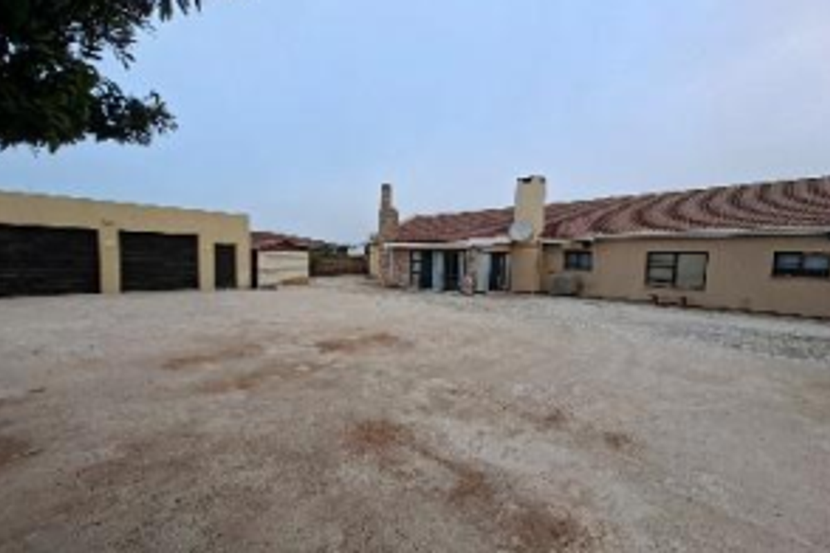Rear view of the property featuring a tiled roof, chimney, and a large concrete driveway area leading to a detached garage.