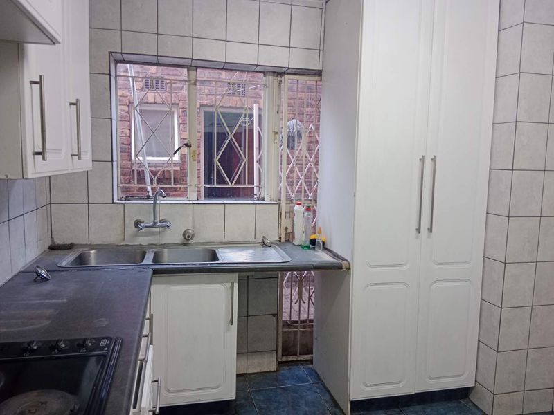 A functional kitchen featuring white cabinetry, double sink, dark laminate countertops, and tiled splashbacks, with direct access to an exterior security gate.