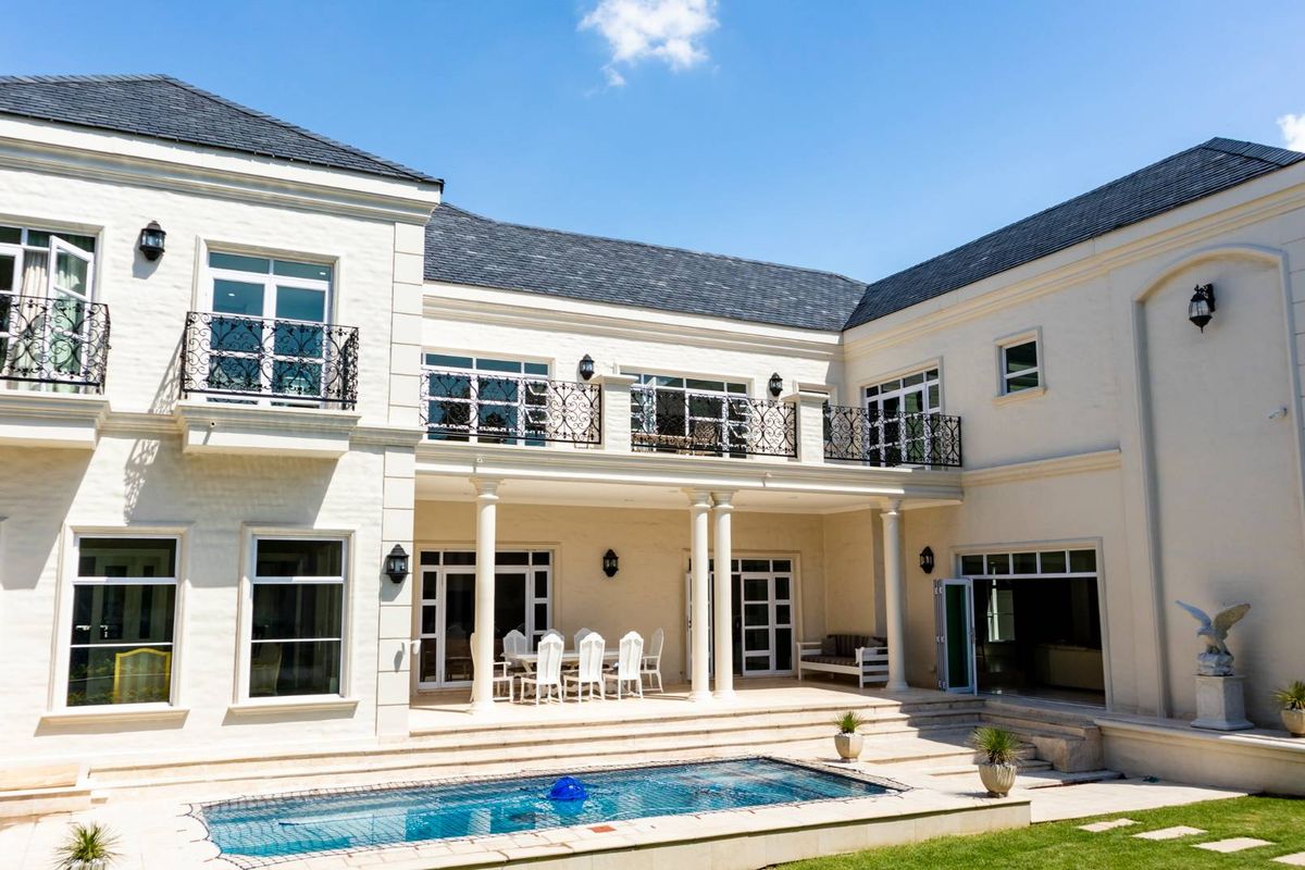 A grand rear elevation featuring a covered patio, upper-level balconies with wrought iron railings, and a swimming pool set against a classic architectural facade.