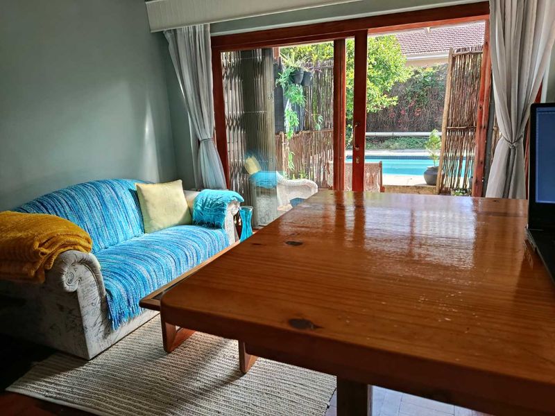 A living room featuring wooden flooring and large sliding glass doors that provide direct access to an outdoor patio and pool area.