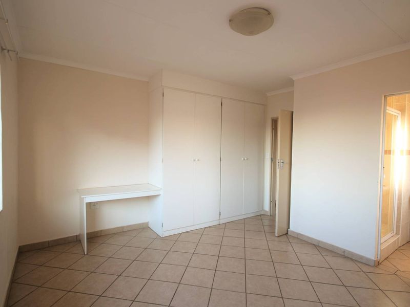 A clean, empty bedroom featuring tiled flooring, built-in cupboards, and direct access to an en-suite bathroom.