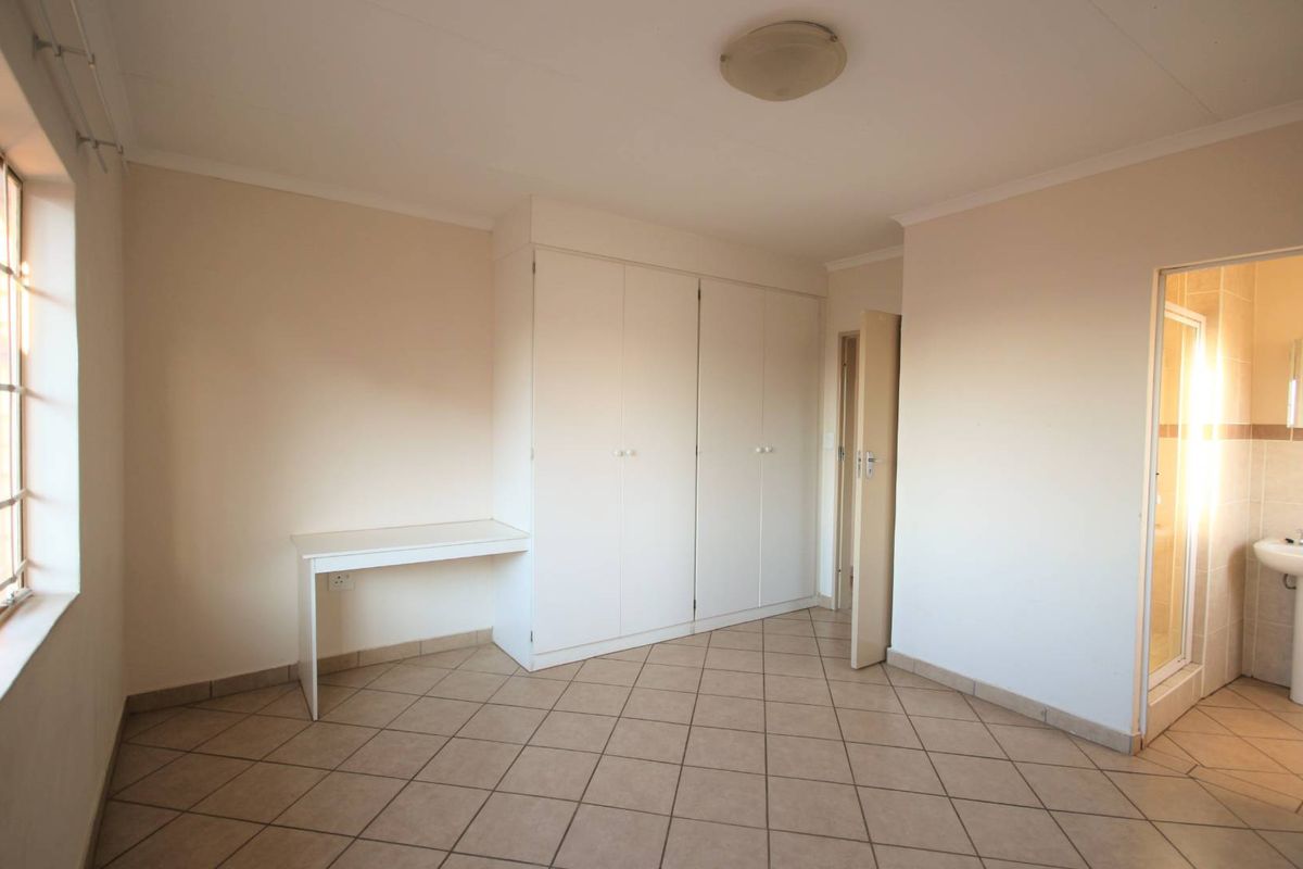 A clean, empty bedroom featuring tiled flooring, built-in cupboards, and direct access to an en-suite bathroom.