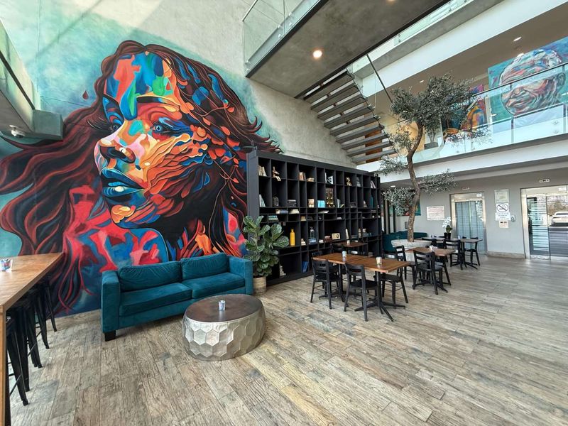 Modern open-plan office lobby featuring a striking feature wall mural, floating staircase with glass balustrade, and contemporary wood-look tile flooring.