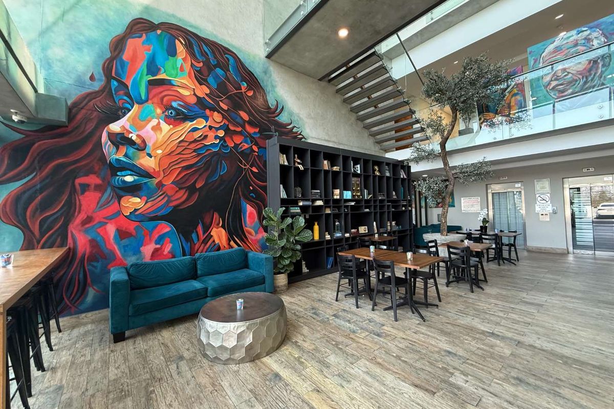 Modern open-plan office lobby featuring a striking feature wall mural, floating staircase with glass balustrade, and contemporary wood-look tile flooring.