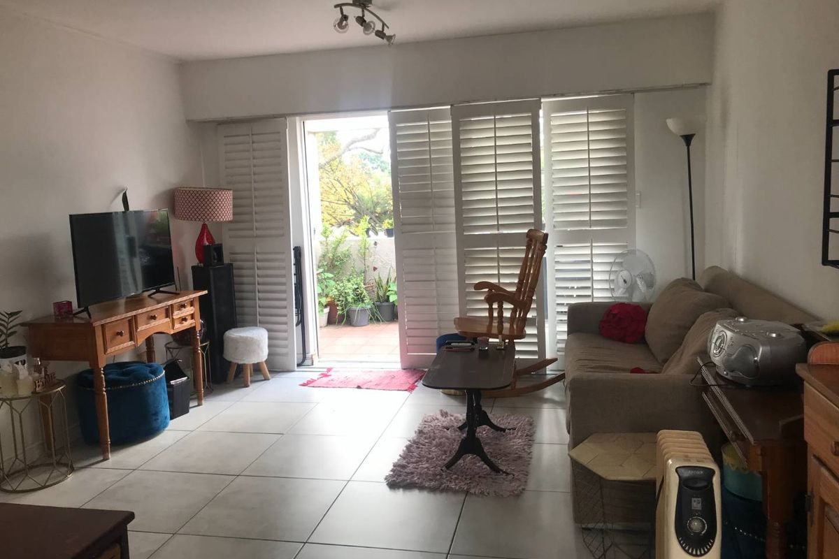 A living room featuring large white plantation shutters opening onto a private balcony, with neutral floor tiles throughout.