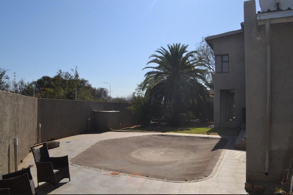 Rear exterior view featuring a paved patio area, a covered swimming pool, and a garden with a large palm tree.