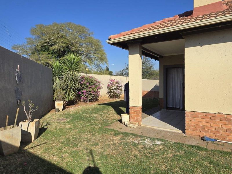 Rear view of the townhouse featuring a covered patio, brick and plaster facade, tiled roof, and a private garden enclosed by a perimeter wall.
