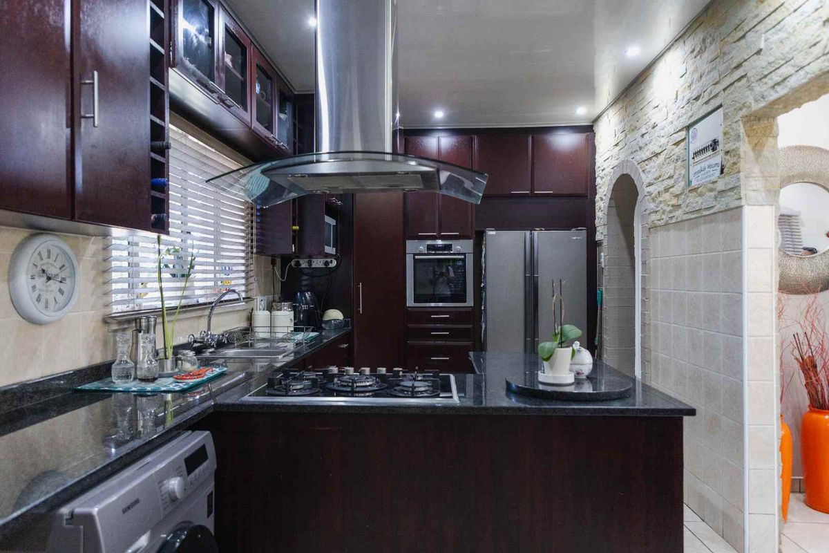 A well-appointed kitchen featuring dark wood cabinetry, granite countertops, a built-in oven, gas hob, stainless steel extractor fan, and a stone-clad feature wall.