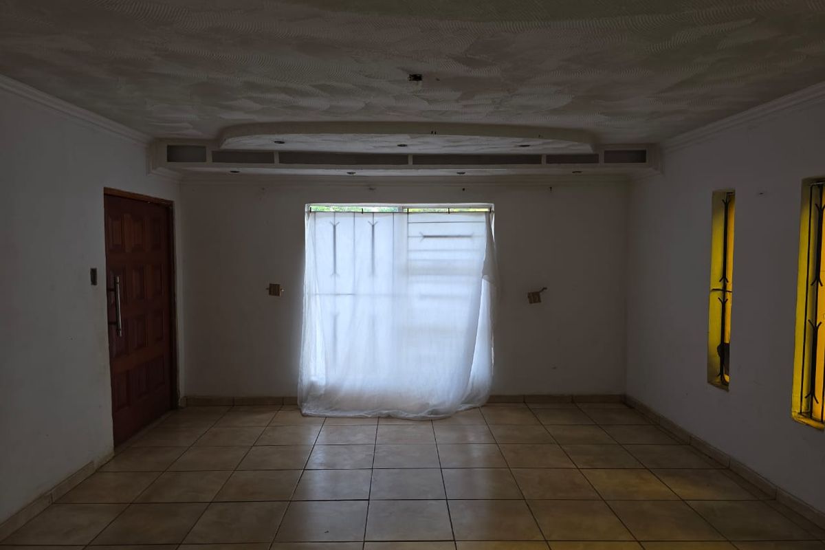 An empty living room featuring tiled flooring, a decorative recessed ceiling, and security bars on the windows.