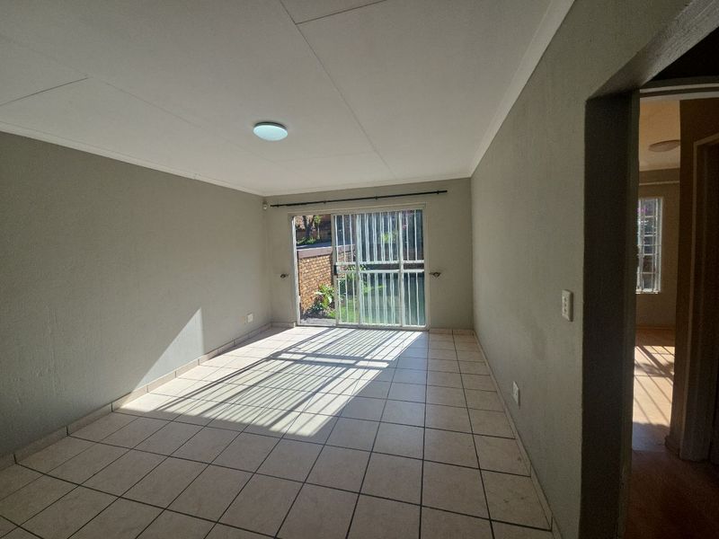 An empty living room featuring tiled flooring and a sliding glass door with a security gate, providing direct access to the outdoor area.