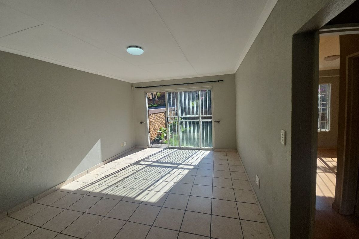 An empty living room featuring tiled flooring and a sliding glass door with a security gate, providing direct access to the outdoor area.