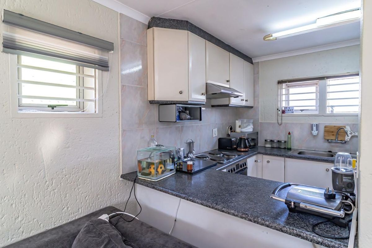 Functional kitchen featuring built-in cabinetry, laminate countertops, an electric hob with extractor fan, and tiled backsplash with security bars on the windows.
