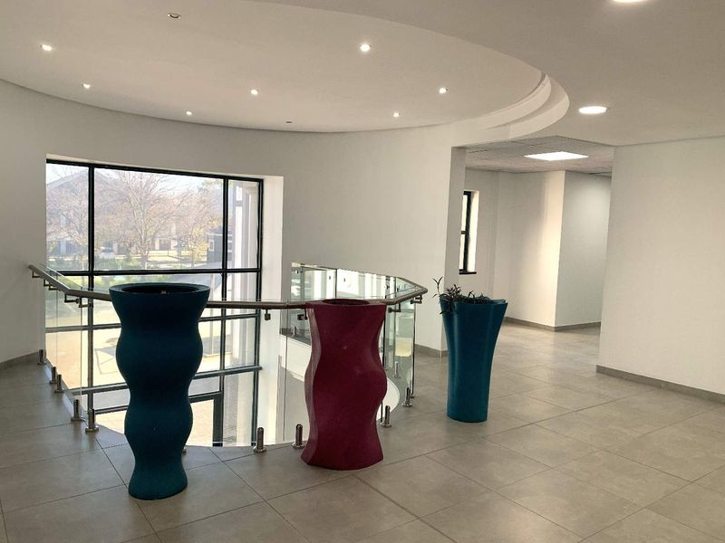 Spacious office hallway featuring tiled flooring, a modern glass balustrade, and large windows providing ample natural light.