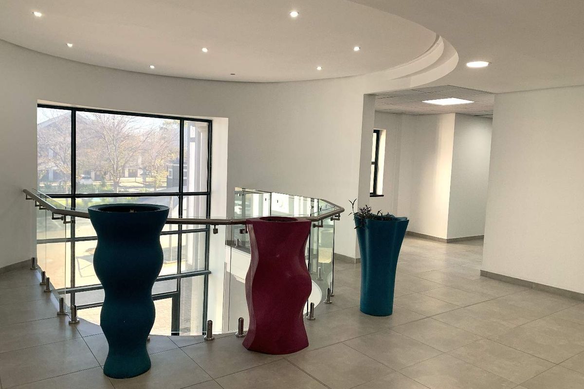 Spacious office hallway featuring tiled flooring, a modern glass balustrade, and large windows providing ample natural light.