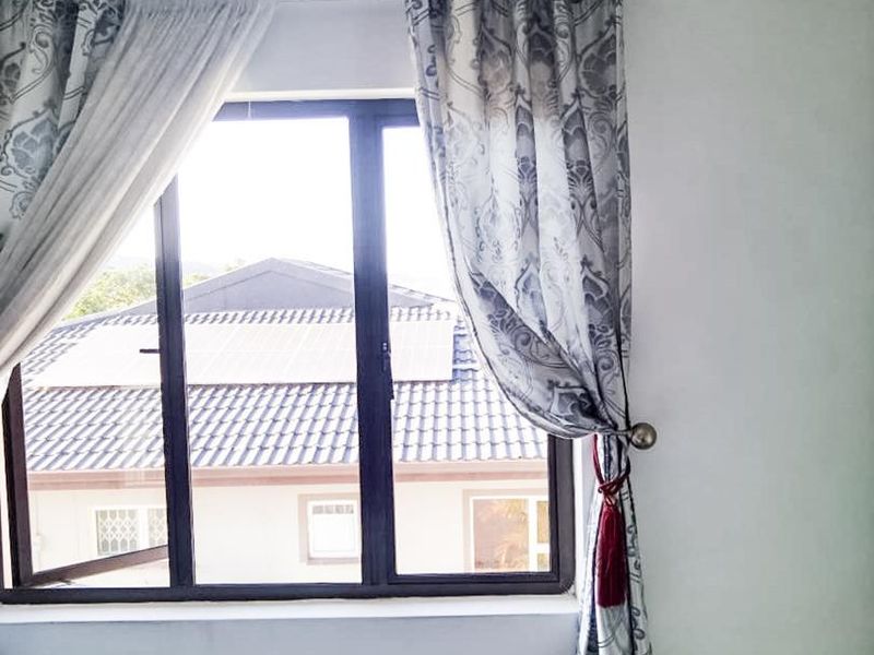A bright bedroom featuring a dark aluminium window frame and integrated ventilation, offering a view of the surrounding residential area.