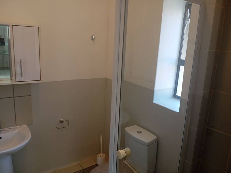 A functional bathroom featuring a pedestal basin, toilet, and a glass-enclosed shower, finished with neutral wall paint and tiled flooring.