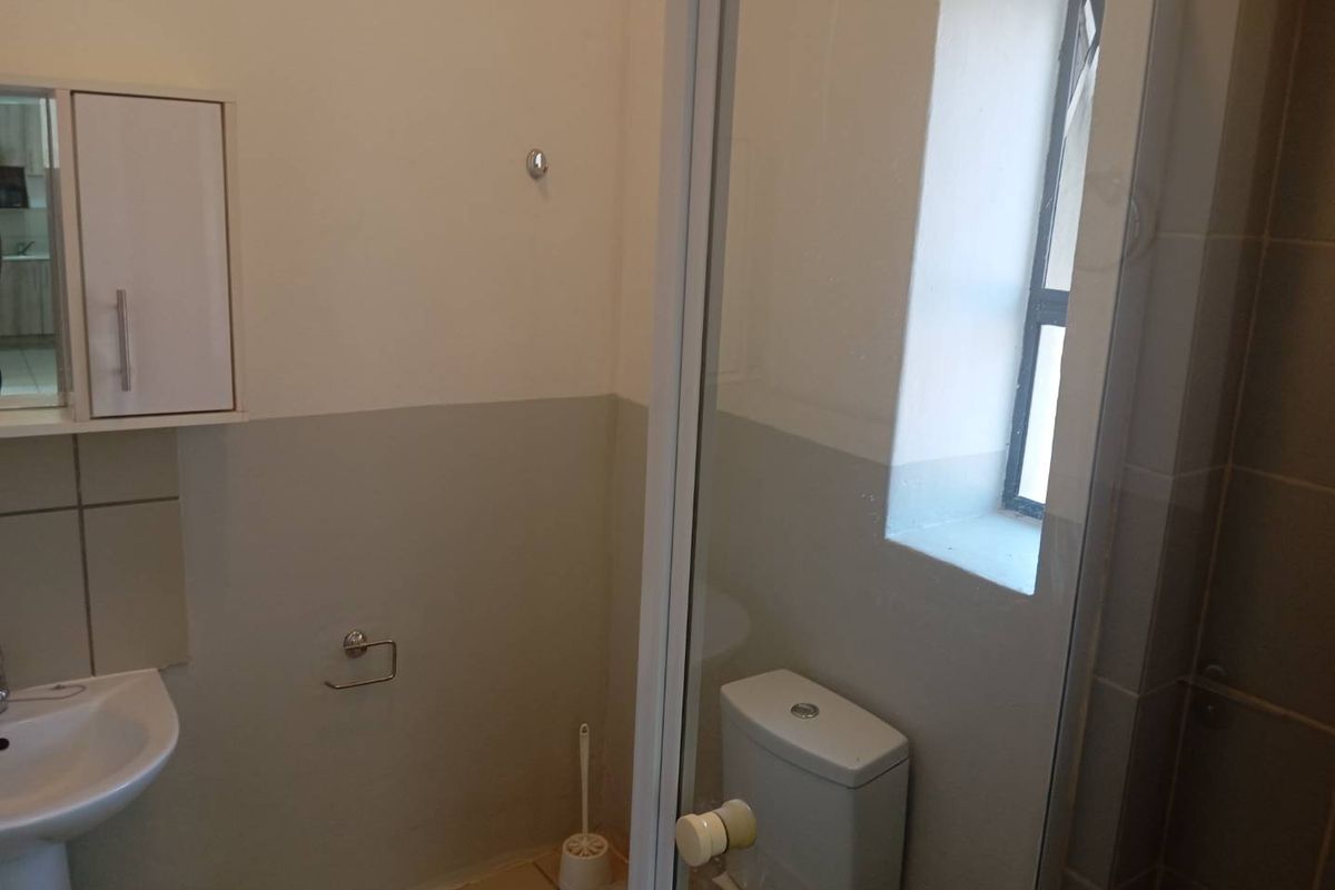 A functional bathroom featuring a pedestal basin, toilet, and a glass-enclosed shower, finished with neutral wall paint and tiled flooring.