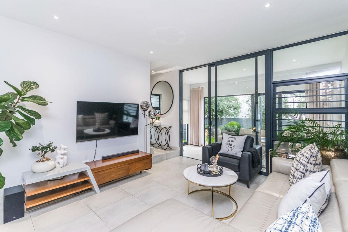 Modern open-plan living area featuring large format floor tiles, recessed downlighting, and expansive glass sliding doors providing seamless access to the outdoor patio.
