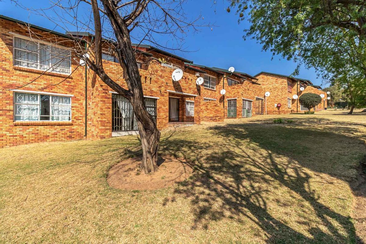 Exterior view of a multi-unit apartment complex featuring face-brick facades, security bars on windows, and a shared communal garden area.