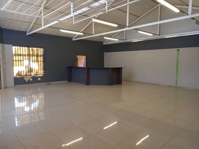 Spacious open-plan industrial unit featuring high exposed steel roof trusses, polished tiled flooring, and a built-in service counter.