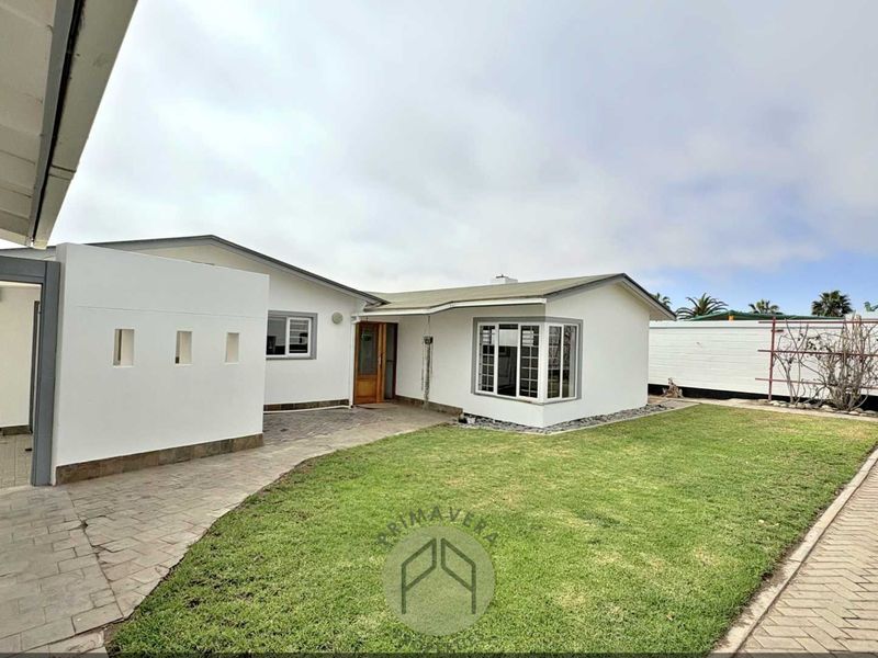 Rear view of the property featuring a paved patio area, a well-maintained lawn, and a bay window overlooking the garden.
