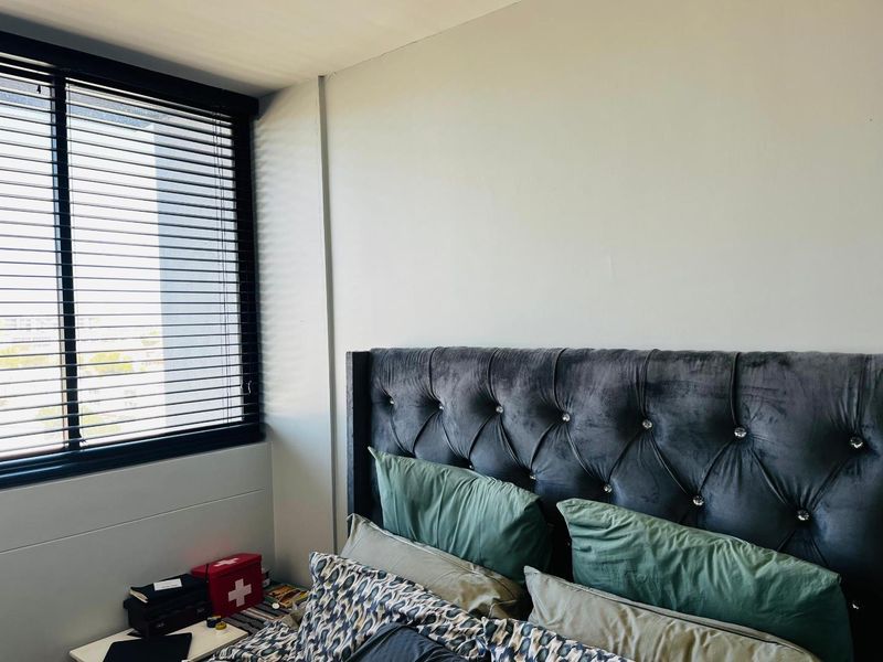A bedroom featuring a large window with dark venetian blinds, providing natural light and a view.