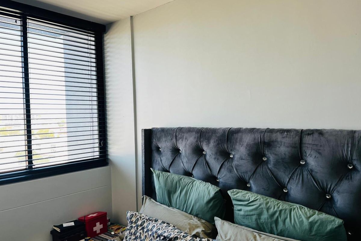 A bedroom featuring a large window with dark venetian blinds, providing natural light and a view.