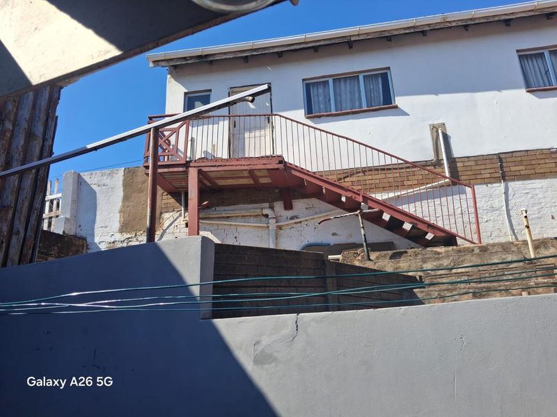 Rear exterior view of the property featuring an external metal staircase leading to an upper level, with visible wear on the facade and boundary wall.