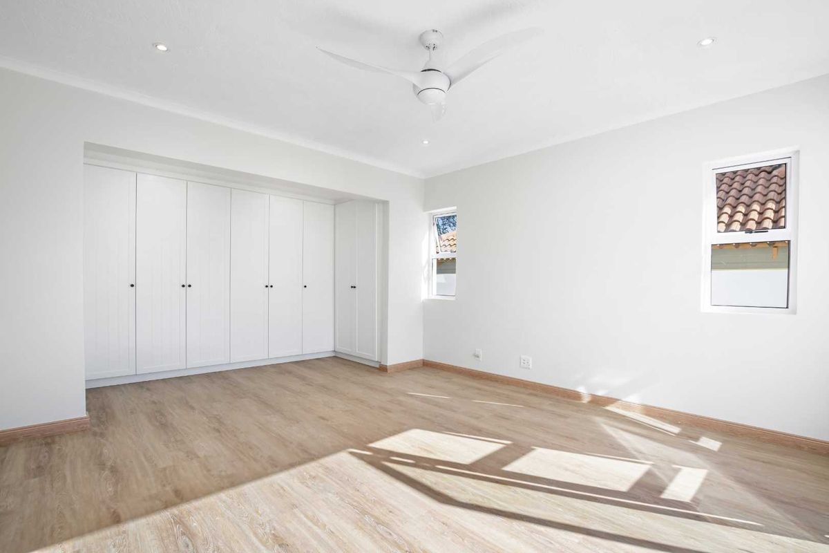 A bright and spacious bedroom featuring light wood-look flooring, built-in floor-to-ceiling cabinetry, and a modern ceiling fan.