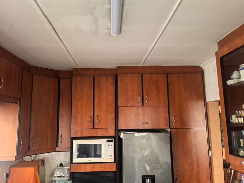 A kitchen area featuring dated wood-finish cabinetry and a built-in microwave, showing signs of ceiling water damage and wear.