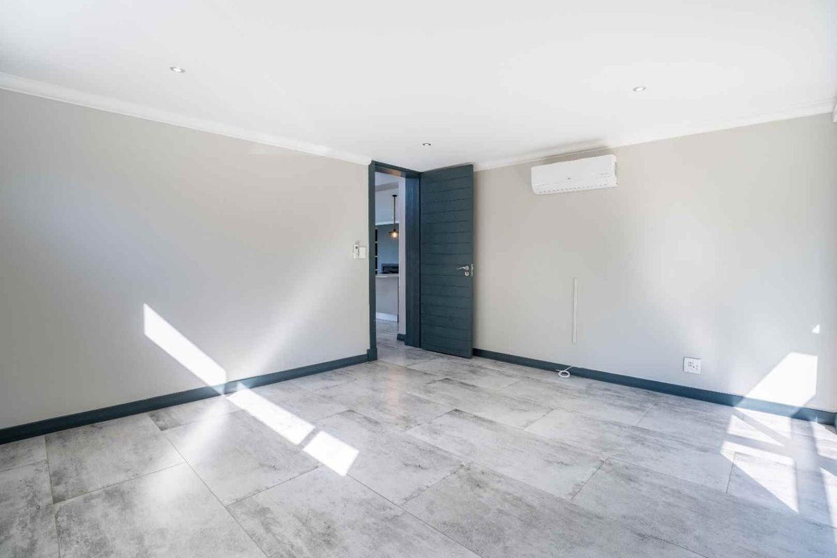A bright, empty bedroom featuring modern grey tiled flooring, neutral walls, recessed lighting, and a wall-mounted split-system air conditioning unit.