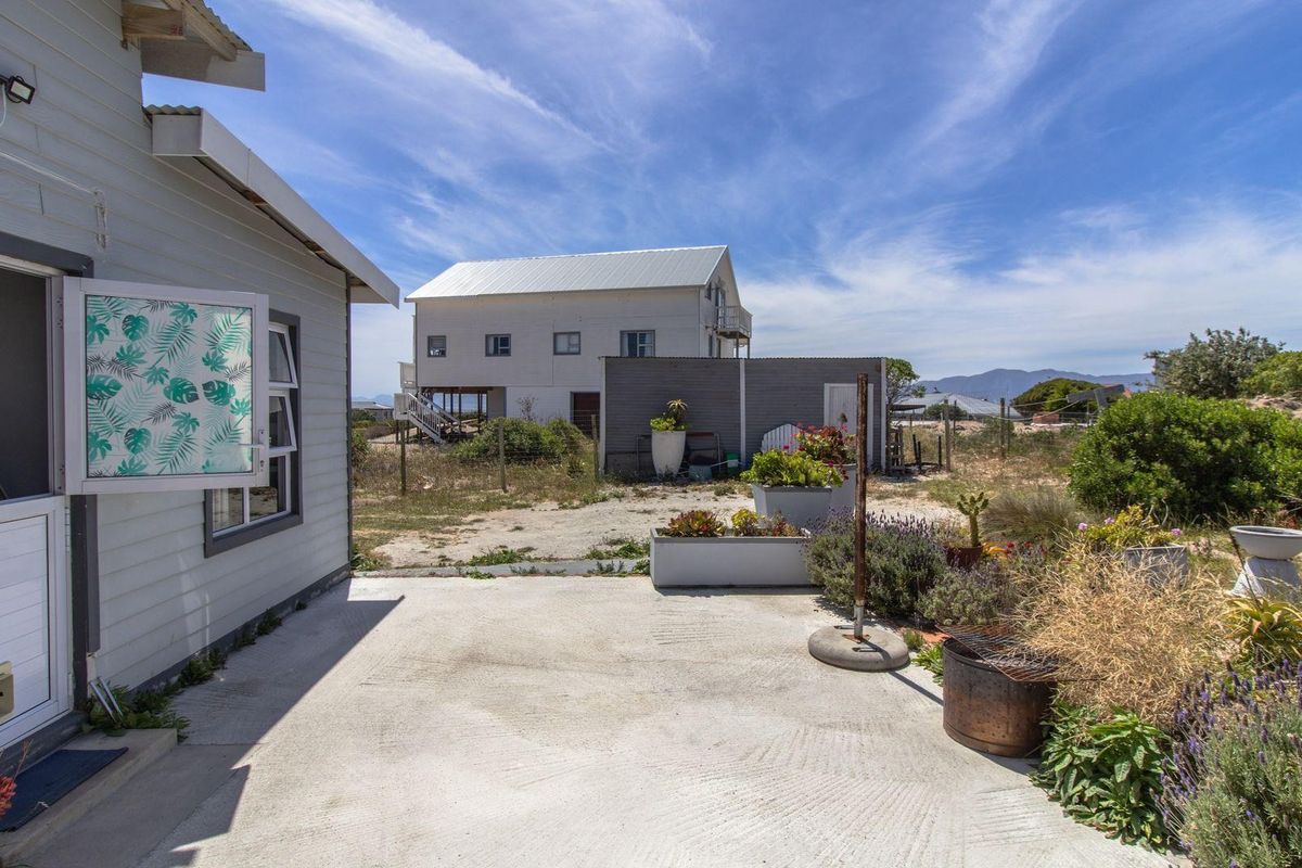 A view of the rear exterior area featuring a concrete patio, landscaped garden beds, and a view towards a neighboring property.