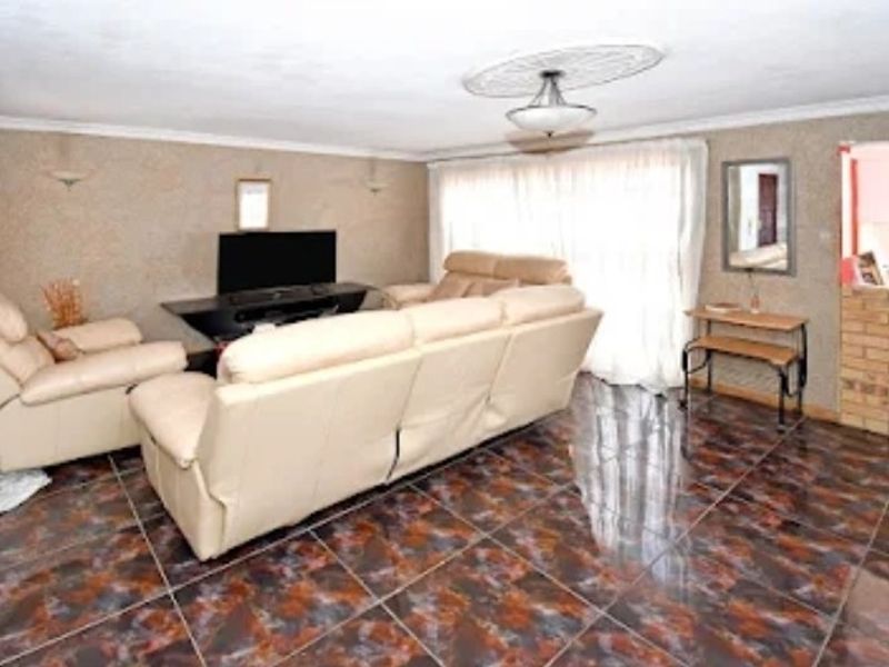 Spacious living room featuring dark patterned ceramic floor tiles, a decorative ceiling rose, and a brick feature wall with access to an outdoor area.