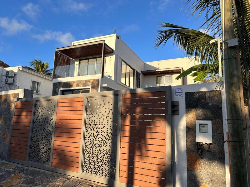 Modern two-story house facade featuring a decorative metal and timber gate, stone cladding, and a glass-railed balcony.