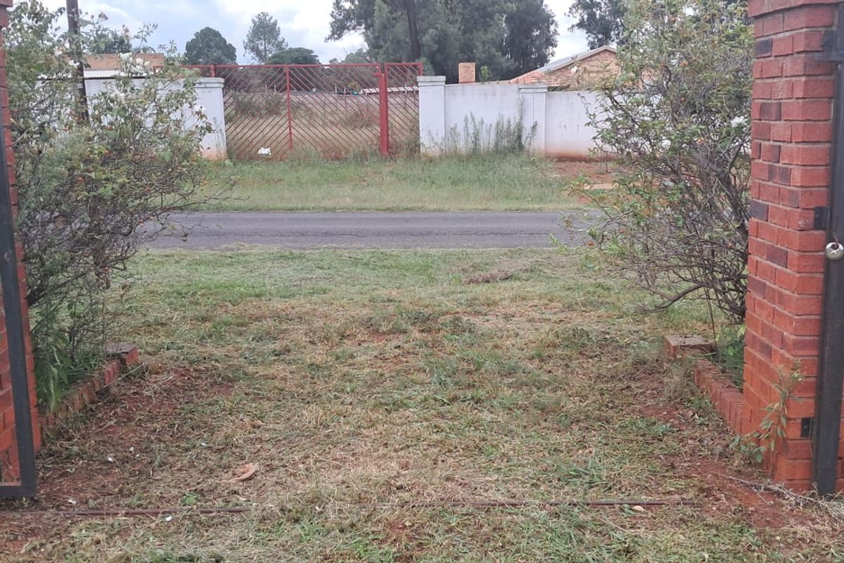 View of the property entrance featuring brick gate pillars and a metal gate frame, opening onto a vacant residential plot.