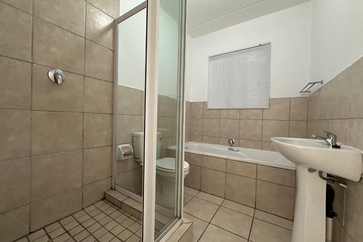 A functional bathroom featuring a separate shower enclosure, a built-in bathtub, and a pedestal basin with neutral wall and floor tiling.
