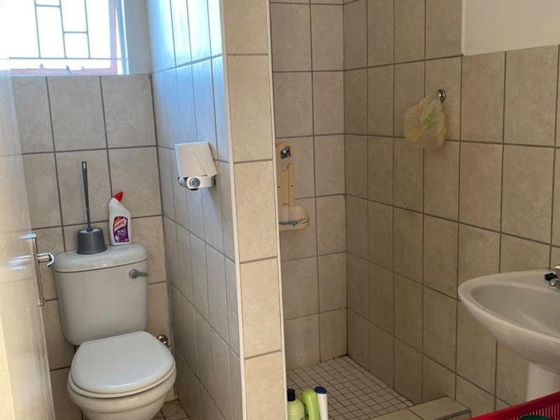 A functional bathroom featuring a shower cubicle, pedestal basin, and toilet with neutral wall and floor tiling.
