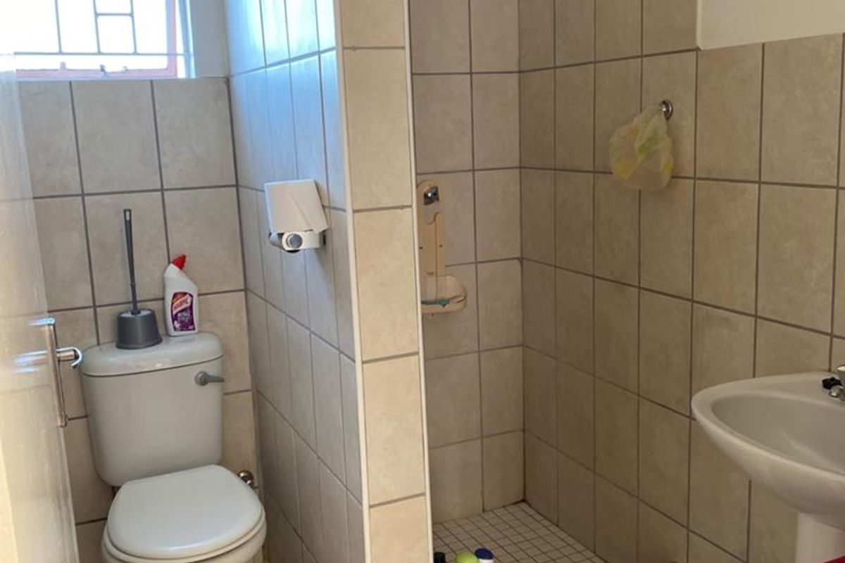 A functional bathroom featuring a shower cubicle, pedestal basin, and toilet with neutral wall and floor tiling.