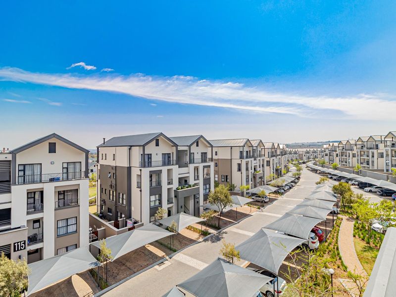 Aerial view of a modern residential complex featuring multi-story apartment buildings, paved driveways, and covered parking bays with shade cloth structures.