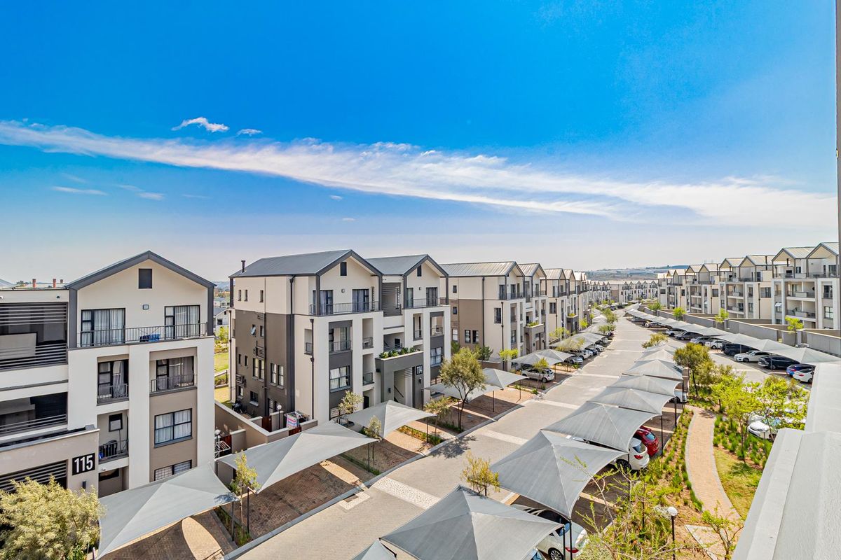 Aerial view of a modern residential complex featuring multi-story apartment buildings, paved driveways, and covered parking bays with shade cloth structures.