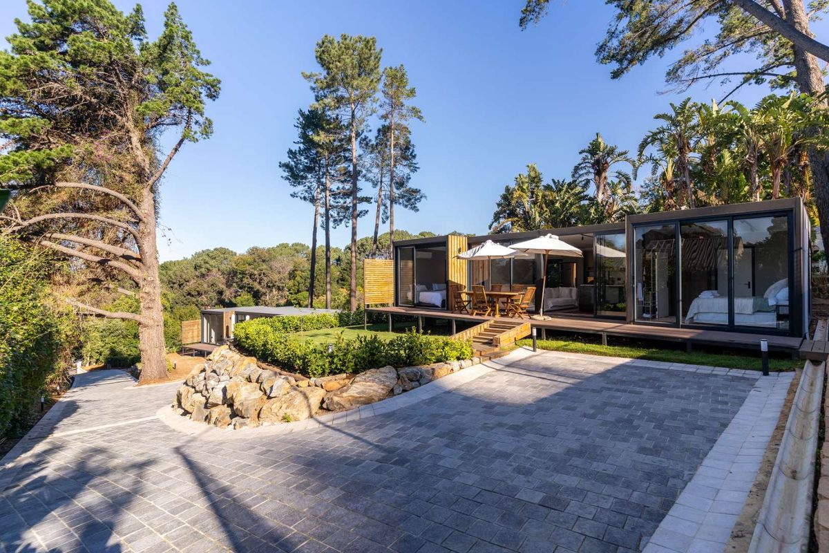 Modern modular home featuring extensive timber decking, large sliding glass doors, and a paved driveway set within a landscaped, wooded environment.