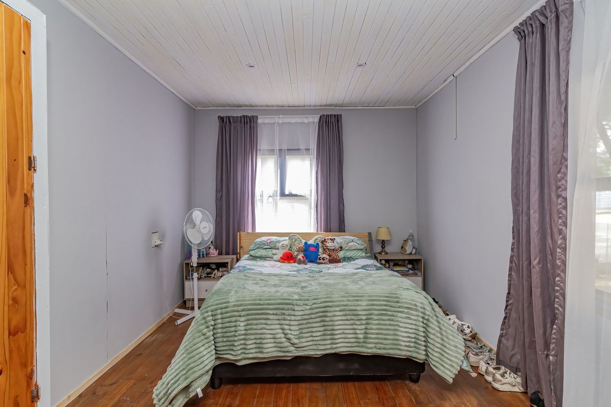 A bedroom featuring timber flooring and a tongue and groove ceiling, providing a functional space with potential for cosmetic updates.