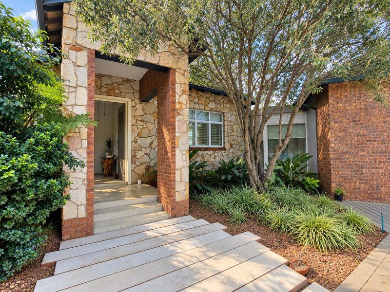 Attractive front entrance featuring natural stone cladding, brick accents, concrete steps, and a well-maintained landscaped garden area.